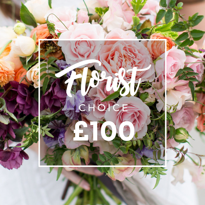 A richly textured, garden-style bouquet is captured in a close, painterly view that emphasises both craft and freshness. Multiple full-bodied pink garden roses dominate the foreground with their ruffled, velvety petals, while soft peach and coral ranunculus sit nearby like warm jewels, their concentric layers creating depth. Darker, plum-toned hellebore-like flowers cluster toward the lower planes of the arrangement, adding a moody, elegant contrast to the pastel blossoms. Whisper-thin sweet peas in pale purple and white drift between the larger blooms, their gentle stripes and delicate forms bringing lightness and scent in the imagination. Creamy white accents and frilly small blooms scatter throughout, catching highlights and lending an airy, romantic punctuation. The foliage is abundant and varied - trailing vines, slender stems and broader seasonal leaves that give the bouquet a natural, freshly gathered silhouette. Superimposed across the centre of the flowers is a clean white rectangular frame containing script text that reads 'Florist Choice', with a smaller uppercase 'CHOICE' below, and a large '?100' in bold sans-serif numerals at the bottom of the block, clearly communicating the florist-selected arrangement and price tag. A pair of hands supports the bouquet from below; a faint pale sleeve and softly blurred clothing in the background keep attention on the floral textures. As prepared by local florists near Nine Elms and the New Covent Garden Market, including pieces made for Florist Nine Elms on request, the bouquet feels bespoke and tactile - ideal for anniversaries, intimate weddings or as a thoughtful luxury gift that nods to the neighbourhood's riverside charm.
