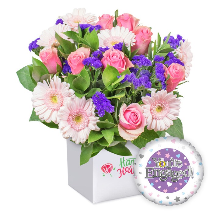 A hand-tied celebration bouquet sits in a square white box, a modern, elegant presentation that speaks of thoughtful planning and festive cheer. The arrangement showcases bold pink roses, their petals opening in a gentle cascade of romance, nestled among light pink gerbera daisies with crisp white edges and soft yellow centers that radiate sunshine. Dotted throughout are clusters of vibrant purple statice, providing vivid color pops and textural contrast, while generous green foliage threads through the bouquet, lending a lively, garden-fresh feel. The container-a clean white square-features a discreet logo with a red rose outline and green script, signaling quality and locality without shouting. To the lower right, a glossy round foil balloon celebrates the moment, its design centered on a purple circle framed by a white ring dotted with pastel hearts and tiny silver stars, the message You're Engaged! glimmering in silver. This complete engagement gift exudes happiness, romance, and forward-looking joy, a beautiful way to mark a couple's milestone in Nine Elms and the surrounding boroughs, with dependable delivery options to satisfy celebrants and friends.