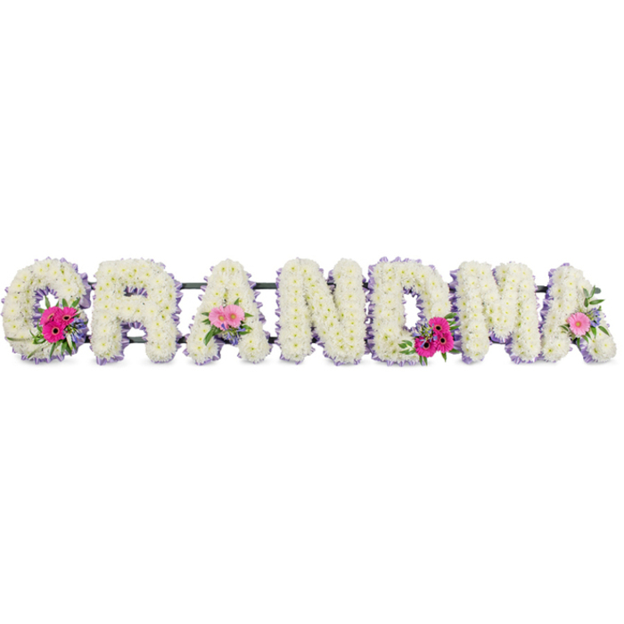 In this floral funeral tribute, the word GRANDMA stretches across the frame in a sequence of large, padded letters, each completely clad in immaculate white chrysanthemums. The blooms are clustered so densely that they form a smooth, almost quilted surface, their rounded petals overlapping like tiny feathers. Around the edge of every letter, a delicately pleated band of light lilac ribbon creates a soft outline, introducing a subtle hint of colour that feels soothing rather than bold. The ribbon's gentle sheen catches the studio lighting, giving the piece a refined, finished look. At three key points on the tribute-the opening G, the middle A, and the closing A-small posies are set into the chrysanthemums, as if gently tucked into a blanket. These feature bright pink gerbera daisies with radiating petals, soft pink roses in varying stages from bud to full bloom, and sprigs of fresh greenery that arc outwards, adding texture and a sense of life. The greens are deep and glossy, contrasting beautifully with the white base and pastel tones. The arrangement sits against a plain, light background, illuminated by diffused light that emphasises the chrysanthemum petals and the soft folds of the ribbon without casting harsh shadows. As a piece that could be created by Florist Nine Elms for a service at a local crematorium or a quiet gathering near Vauxhall and the riverside paths, it feels both personal and dignified. The tribute conveys warmth, respect, and a sense of gentle continuity-flowers standing in for words that are often too hard to say, offering comfort to a family saying goodbye to a beloved grandmother.