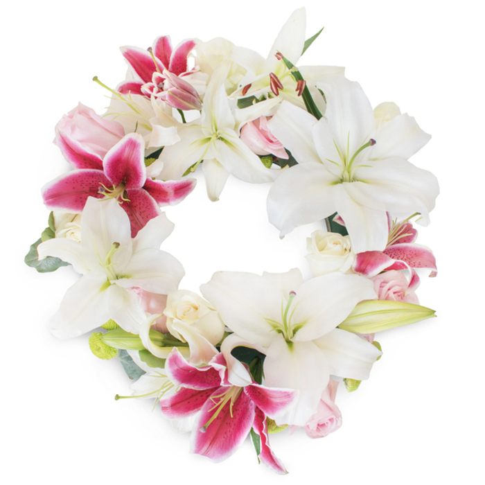 Expertly arranged for memorial gatherings across Nine Elms, this lush funeral wreath is encircled by pristine white Oriental lilies, their star-shaped petals either gracefully open to reveal greenish-yellow stamens or just tenderly budding. The purity of these white blooms creates a tranquil foundation, their smooth surfaces glowing softly against the clean white backdrop. Threaded through the arrangement are bold, fuchsia-pink Stargazer lilies-each bloom showcasing vivid magenta petals dusted with darker pink speckles, infusing the wreath with vibrant contrast and undeniable depth. Interspersed between the lilies, clusters of creamy white and blush pink roses provide a romantic softness; some roses remain tightly clustered, while others gently bloom, unfolding ruffled petals reminiscent of love's gentle transitions. Subtle hints of fresh green, perhaps eucalyptus or lily foliage, peek out just so, lending a natural structure and verdant undertone that echoes the nearby gardens and tree-lined streets of Nine Elms. Completing the full, unbroken circle, the meticulous placement of each bloom ensures the arrangement embodies unity, continuity, and the everlasting cycle of life. Bathed in gentle daylight, the design exudes an air of peace, grace, and reverence, perfectly attuned for heartfelt farewells, funeral services, or moments of quiet reflection by the Thames. This tribute, crafted with local care and sensitivity, offers comfort and enduring beauty to those seeking to honor and remember a loved one.