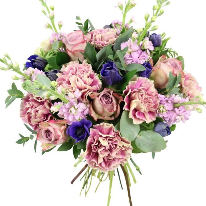 Captured on a clean white background, this hand-tied bouquet appears as a lush, carefully composed work of floral art, the kind a local florist might prepare for a chic apartment overlooking the Thames in Nine Elms. At the core, large garden roses form a soft, romantic centre in tones of dusty blush, muted mauve, and antique rose. Each bloom is generously petalled, with delicate spirals that open outward, creating a sense of depth and gentle movement. Nestled among them, ruffled carnations bring volume and a tactile quality; they shift from creamy beige and pale pink near the centre to richer rose and fuchsia at their frilled edges, so every petal seems lightly brushed with colour. The design is laced with dramatic accents of deep indigo and royal blue. Some appear as smooth, tulip-like buds, while a notable blue anemone, with its striking inky centre, sits prominently near the front, drawing the eye and adding a sophisticated contrast reminiscent of evening skies over Battersea and Vauxhall. Airy spires of lilac and soft purple stock flowers rise up through the bouquet, their small, clustered blossoms bringing both lightness and an almost ethereal, garden-like feel. Framing it all is abundant foliage: glossy dark green leaves that hint at the roses' natural growth, and rounded, silvery eucalyptus that arcs gracefully, suggesting coolness and a fresh, clean aroma. The stems are gathered tightly and left visible at the base, signalling that this is a fresh, high-quality arrangement, ideal for weddings, anniversaries, or springtime celebrations in and around Nine Elms, where elegant, contemporary living meets the charm of classic flowers.