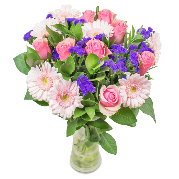 A strikingly arranged bouquet by a Nine Elms florist, set against a pristine white backdrop and presented in a clear glass vase that reveals freshly cut stems and crystal water. The centerpiece features approximately seven to nine soft to mid-tone pink roses, many showing petals elegantly spiralling-from tightly furled buds to those just starting to unfurl-conveying both freshness and natural charm. These roses are gracefully surrounded by five to seven pale pink gerbera daisies, their large, dainty heads and countless radiating petals distinguishing them amidst the ensemble. Bright purple statice, bold and textured, weaves throughout, offering lush contrast and a modern burst of colour. Underpinning the bouquet is abundant deep green foliage, lush and vibrant, enhancing the arrangement's sense of freshness-suggesting a recent arrival from Nine Elms' well-known flower markets. The arrangement, perfect for birthdays, anniversaries, Mother's Day or simply as an expressive decorative accent for a home or office near Vauxhall or the Embassy Quarter, radiates a sense of joy, affection, and refined celebration that defines local floral artistry.