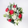 A hand-tied bouquet viewed from above, filled with crimson roses, pink-red carnations, and cloudlike white chrysanthemums, resting as if on a kitchen table in a bright Nine Elms flat. The roses sit at the heart of the design, their deep red, velvety petals spiralling tightly, while the carnations ruffle around them with soft, feathery folds in shades of pinkish red. Around this passionate core, petite white chrysanthemum daisies and airy gypsophila cluster like flecks of fresh snow, bringing an uplifting lightness that softens the stronger colours. Eucalyptus stems thread through the arrangement, their cool, silvery-green leaves adding a contemporary edge that London florists favour, and providing a gentle herbal scent that contrasts the sweeter perfume of the blooms. Rich, tropical foliage in deeper greens frames the entire bouquet, giving it structure and a feeling of fullness without ever appearing stiff or formal. The flowers look freshly gathered, petals unblemished and bright, as if they have just arrived from an early-morning delivery run along the Thames near Battersea Power Station. This bouquet feels like the moment a celebration begins: perfect for setting on a birthday table, welcoming someone home after a long day commuting through Vauxhall, or marking a small but meaningful milestone. Every stem appears carefully placed, but there is still a natural, easy grace to the composition that reflects the relaxed, modern spirit of Nine Elms living, where fresh flowers can instantly turn an urban apartment into a warm and inviting home.